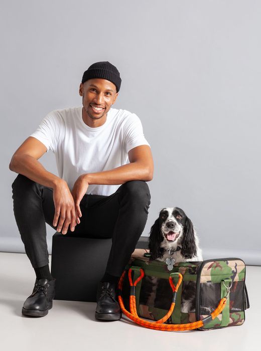 A dog inside a camo and orange pet carrier.