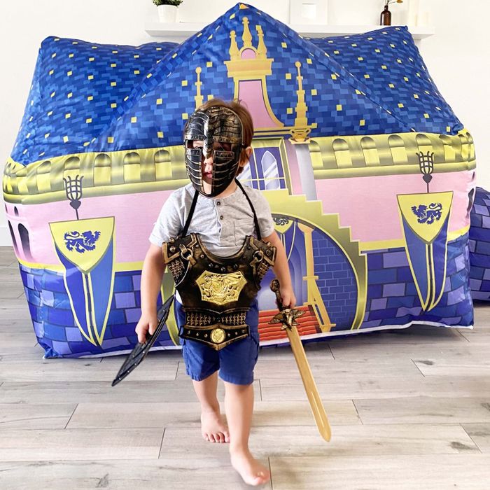 A child dressed in a knight's costume, standing in front of a castle-themed inflatable fort.