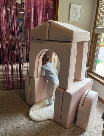 A reviewer’s child playing inside a fort made from stacked cushions.