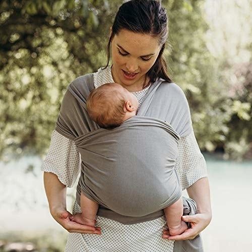 A model wearing a grey baby wrap with a little one snugly secured.
