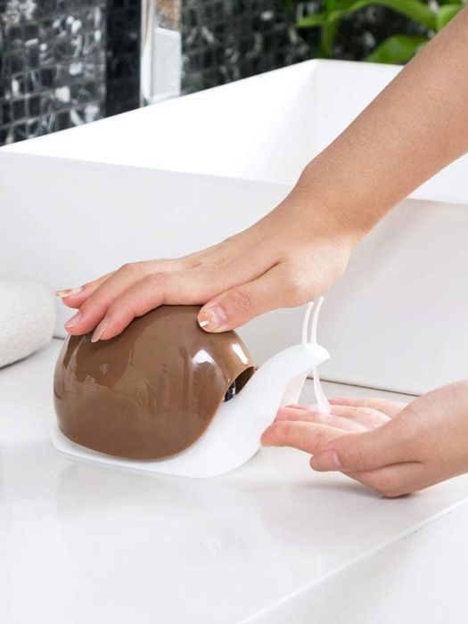 One hand pushing the snail's shell while the other hand dispenses soap from the snail's head.