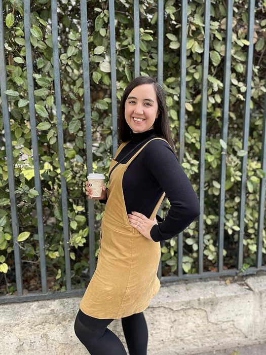 A reviewer is seen in the black sweater layered over a beige overall dress.