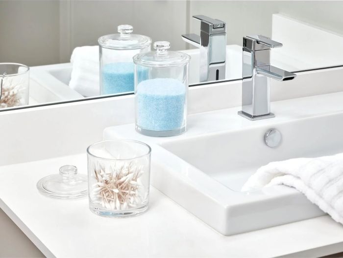 A set of small clear jars with lids placed neatly next to a sink.