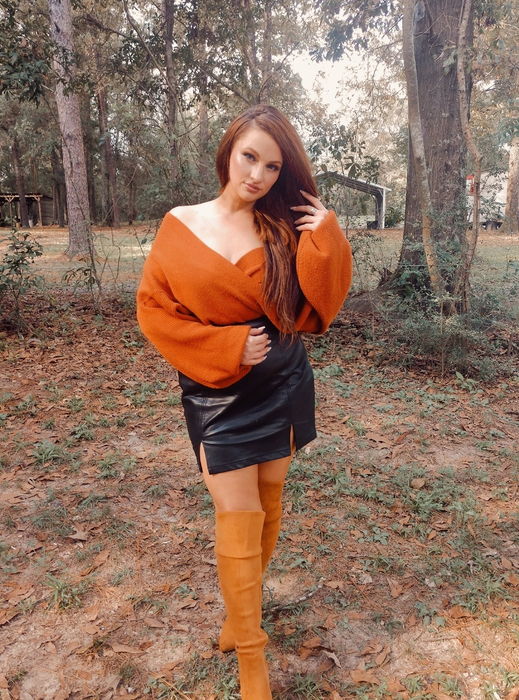 reviewer outdoors styled in an oversized off-the-shoulder sweater, paired with a black mini skirt and thigh-high boots
