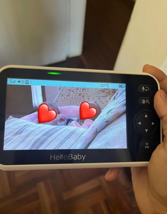 A reviewer holding a HelloBaby video monitor, displaying a peaceful baby sleeping under a cozy blanket.