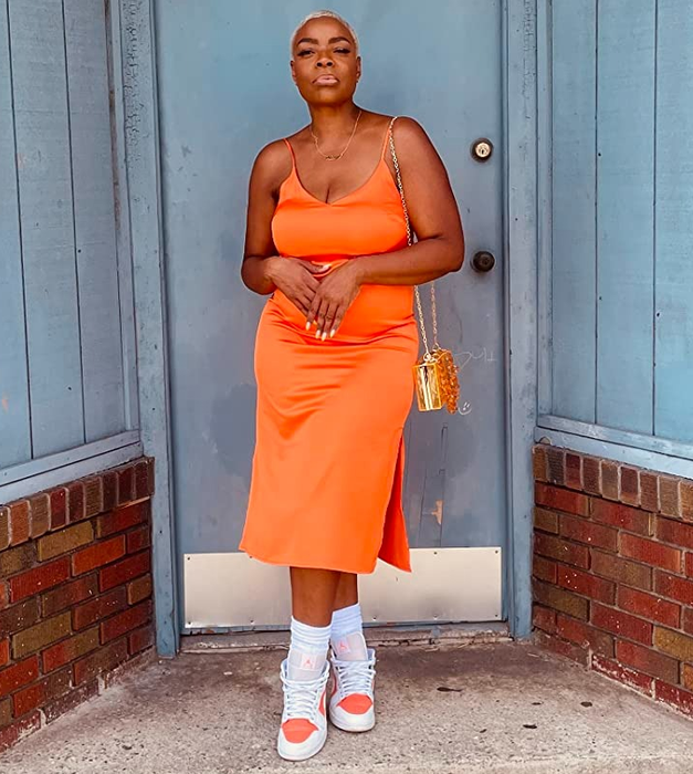 A reviewer dons an orange dress and confidently stands before a blue door