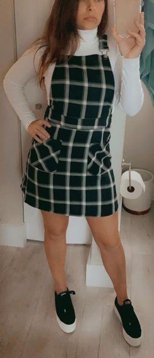 A critic showcasing the green suspender dress adorned with a white plaid pattern