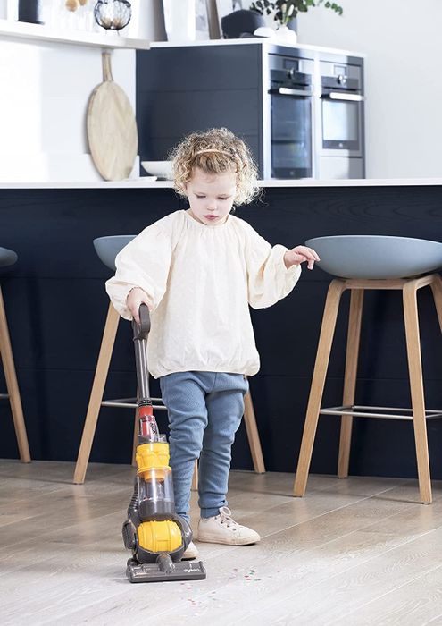 A child playing with a realistic-looking mini Dyson Ball toy vacuum.