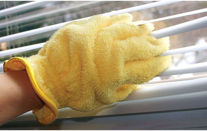 A person wearing the glove and cleaning blinds by sliding their fingers between the slats.