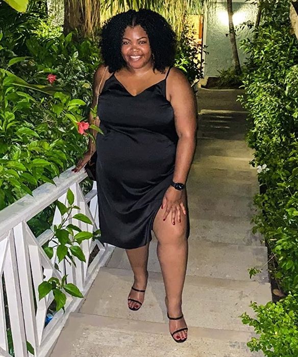 A reviewer in a black dress, paired with strappy sandals, confidently strikes a pose
