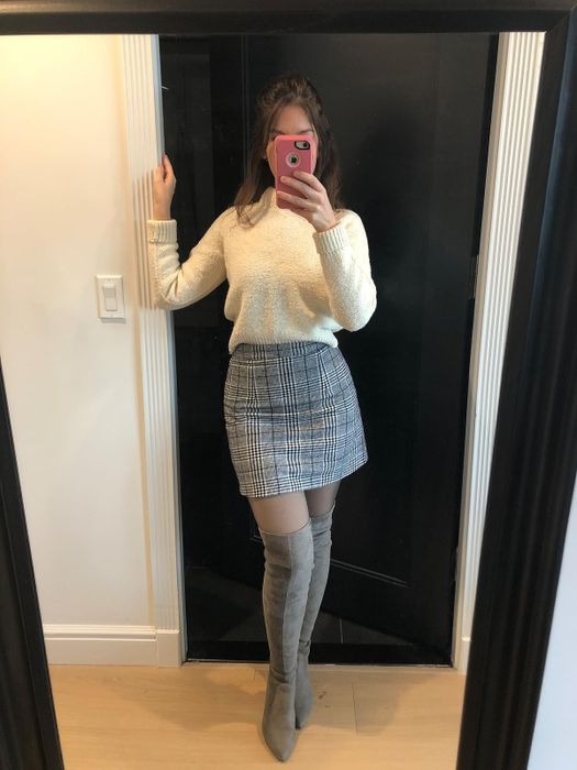 reviewer capturing a mirror selfie, dressed in a white sweater, plaid skirt, and thigh-high suede boots