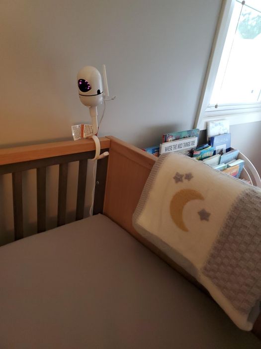 A baby crib with a monitor securely attached to its side.