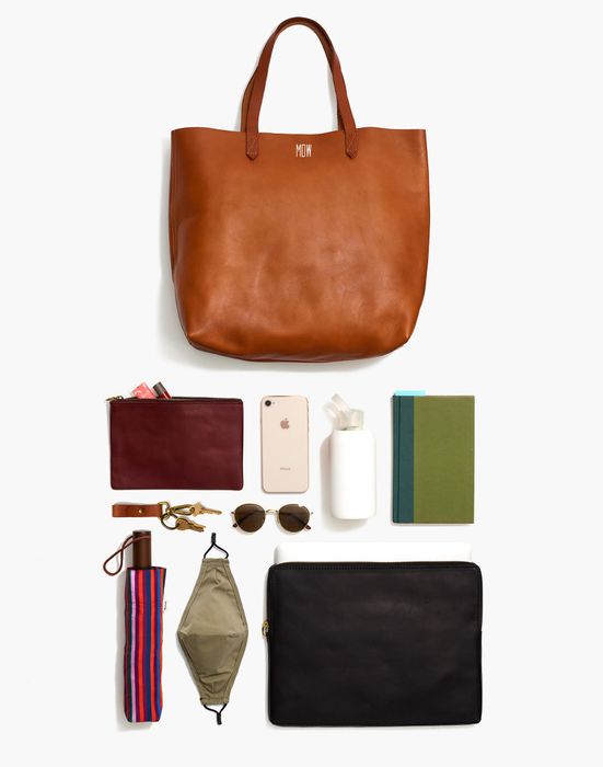 Flat lay of the bag with its contents: a pouch, phone, water bottle, notebook, keys, sunglasses, umbrella, mask, and laptop case.