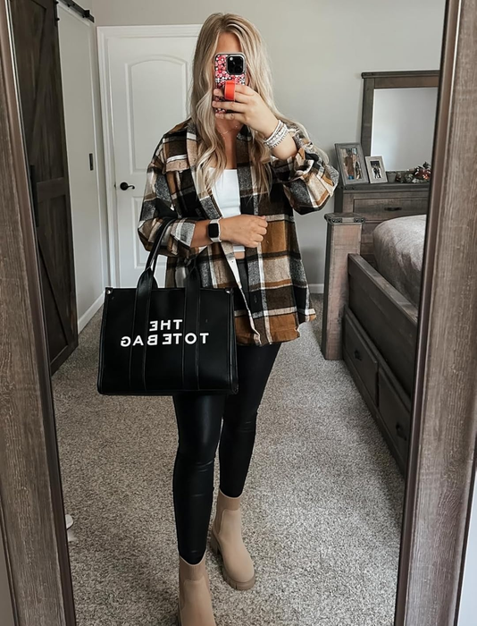 A reviewer captures a mirror selfie in a bedroom, dressed in a brown and black plaid shirt