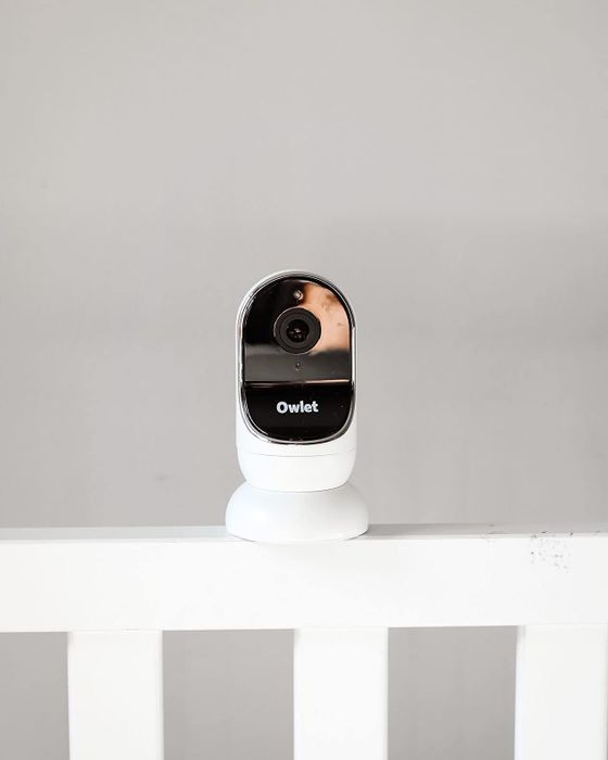 A sleek smart baby monitor mounted on the railing of a white crib.