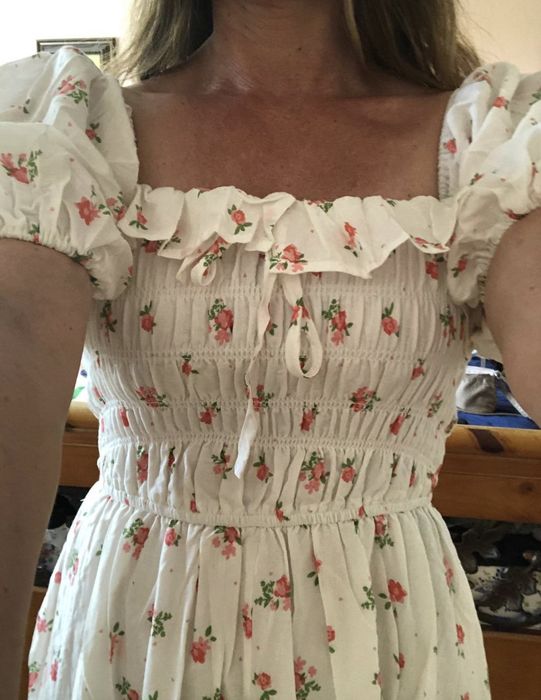 A person wears a floral dress featuring puff sleeves and a ruffled neckline, captured in a photo from the neck to waist
