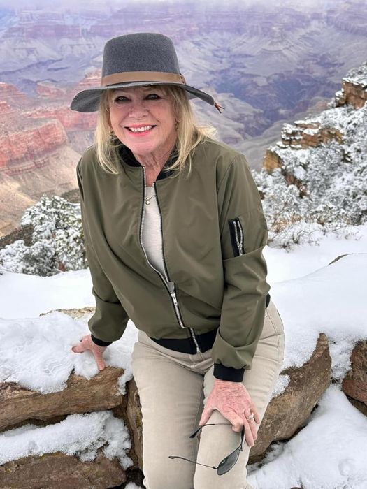 The reviewer strikes a pose on a snow-covered cliff at the Grand Canyon, wearing a stylish green bomber jacket.