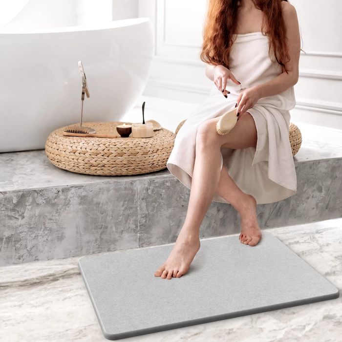 A model sitting on a step beside a bathtub, stepping onto a stone bath mat