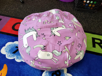 A bean bag chair adorned with playful unicorn prints, sitting on top of a colorful play mat.