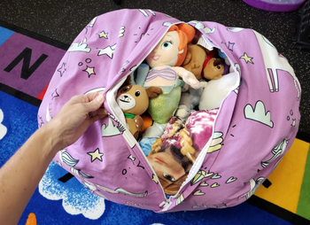A hand opening a plush toy storage bag, revealing a collection of stuffed animals inside.