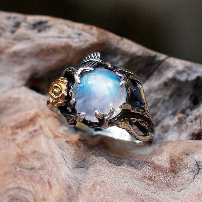 The ring features a mystical band encircling the blue moonstone, intricately designed to resemble dragons.