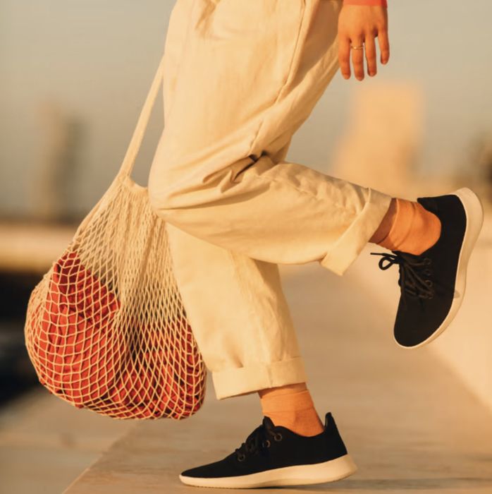 Person walking outside, lifting their heel while wearing black sneakers