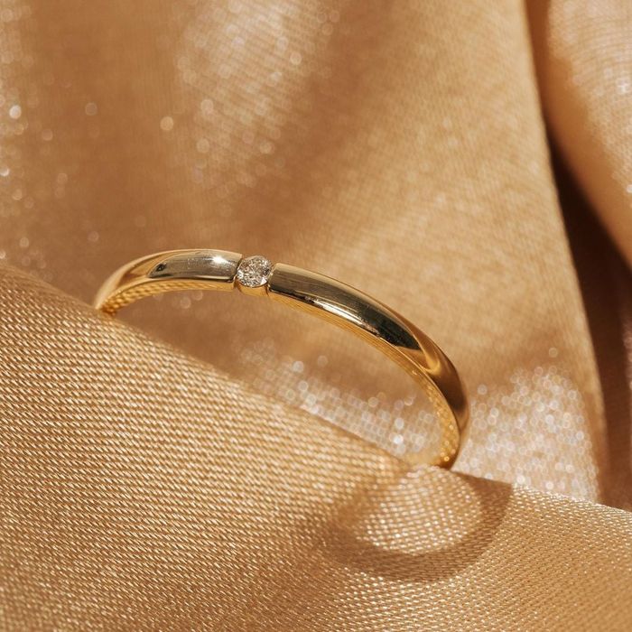 A slender gold band featuring a small, round diamond at its center, radiating elegance and simplicity.