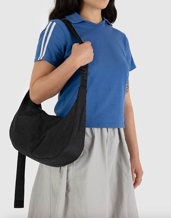 A person in a blue polo shirt and gray skirt carries a black shoulder bag on their left side.