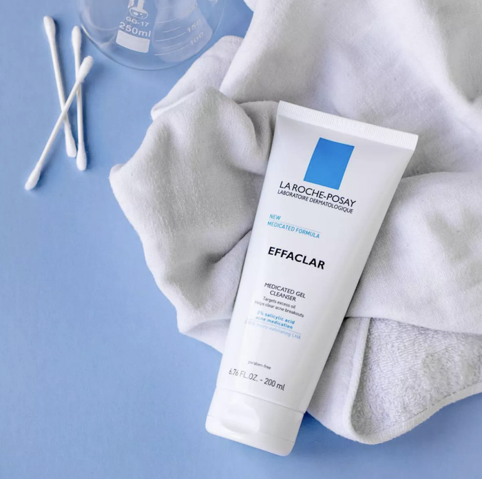 A bottle of face wash resting on a towel atop a blue table