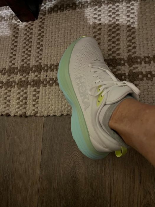 Reviewer wearing white and green sneakers, standing on a patterned floor rug.