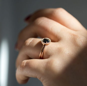 A model showcasing a round engagement ring featuring a black diamond in the center, surrounded by a halo of smaller diamonds