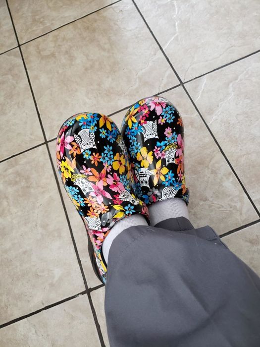 Reviewer in scrubs with crossed ankles, sporting black clogs with a colorful floral design