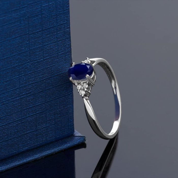A silver ring with a blue sapphire stone in the center, surrounded by three small diamonds
