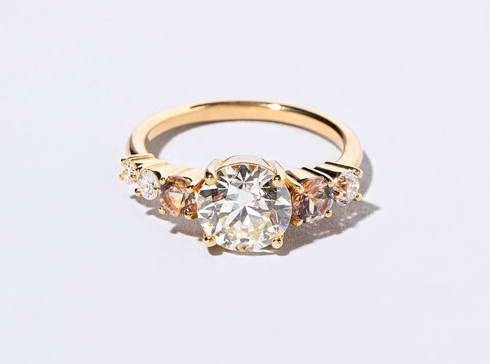 A gold ring with a central diamond, surrounded by smaller gems, set against a white backdrop, exuding elegance and class.