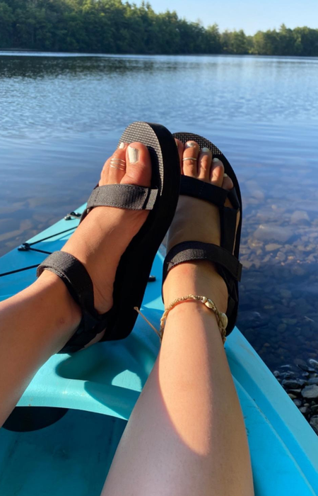 A reviewer’s photo showing a person's feet in black Tevas while kayaking on a lake.