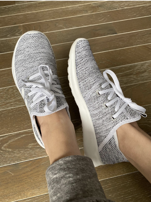 A reviewer showcasing a pair of grey lace-up slip-on sneakers.