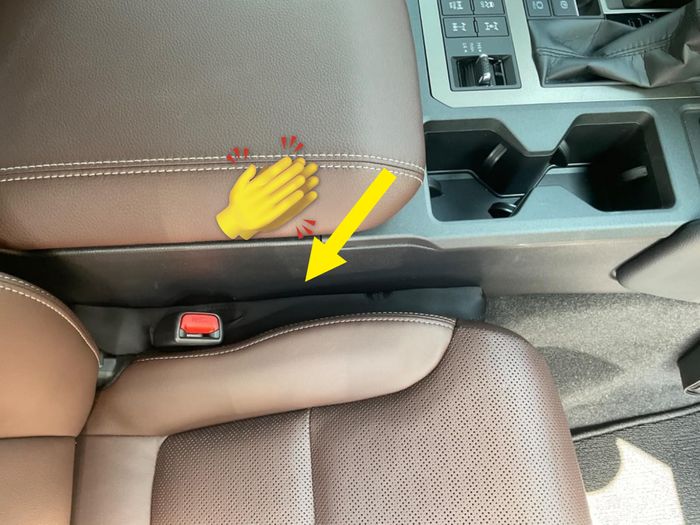 A car seat featuring a seatbelt buckle, a console with cup holders, a gear shift, and visible climate control buttons.