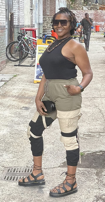 A reviewer poses in a city wearing black sandals, sunglasses, and a sleeveless black top, paired with two-tone cargo pants.
