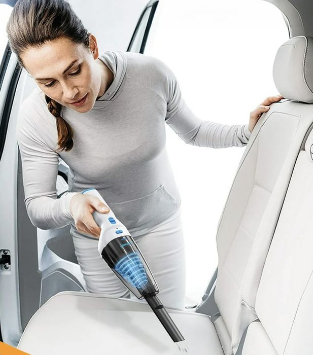 A person using a handheld vacuum to clean the backseat of a car.