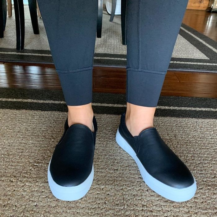 Reviewer showcasing the black slip-on sneakers featuring a white wide sole