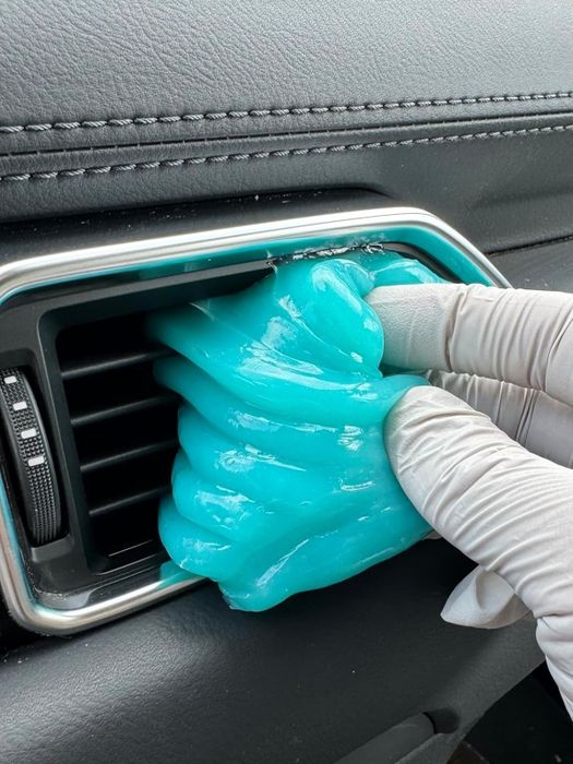 Gloved hands using blue cleaning gel slime to clean the air vents of a car.