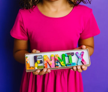 a child holding colorful, marbled crayon letters that spell out a name