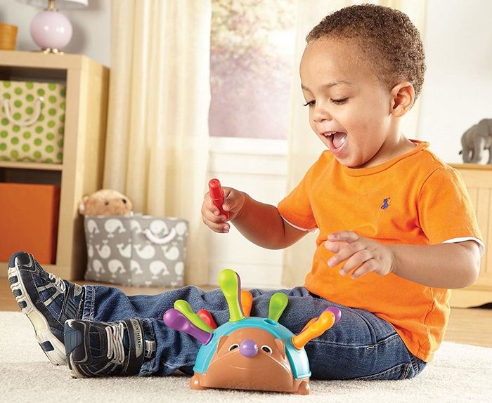 A child model interacting with the colorful plastic pegs of a toy hedgehog