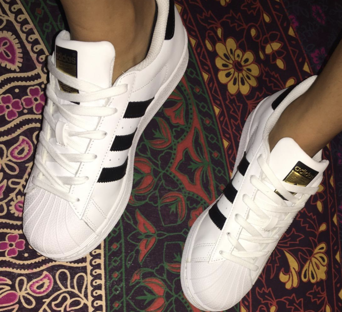 A reviewer wearing white, black, and gold adidas sneakers.