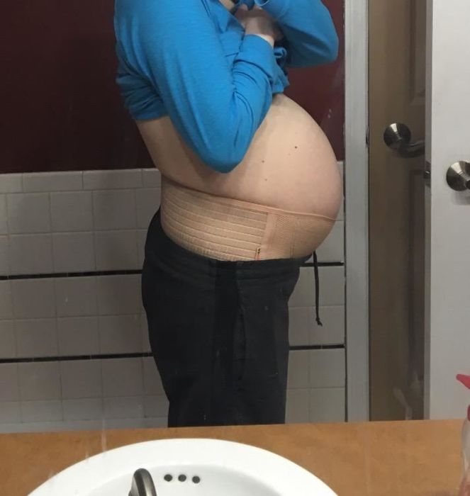 reviewer wearing the pale taupe band with sweatpants right under the bottom of their pregnancy abdomen