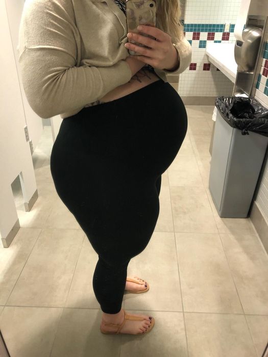 same reviewer lifting their top and cardigan to reveal leggings that comfortably cover their pregnant belly
