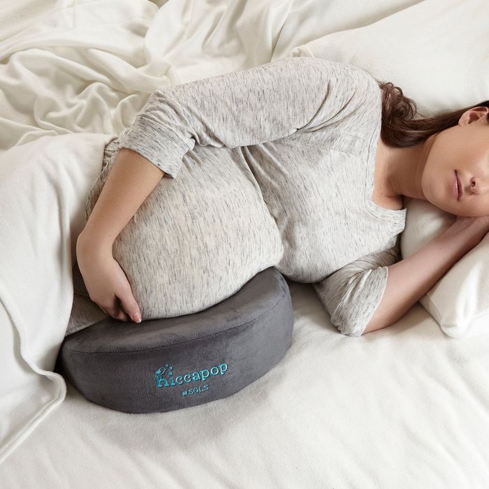 A model resting in bed with a wedge-shaped pillow supporting their pregnancy belly.