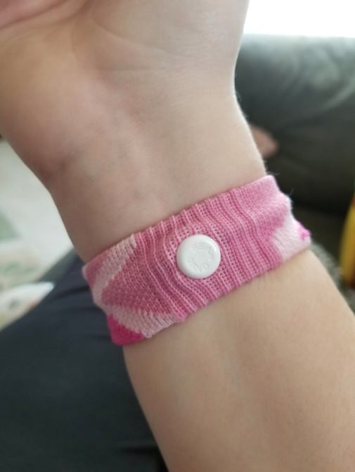 A reviewer wearing the knitted band with a white plastic button that goes over the pressure point on the inside of their wrist
