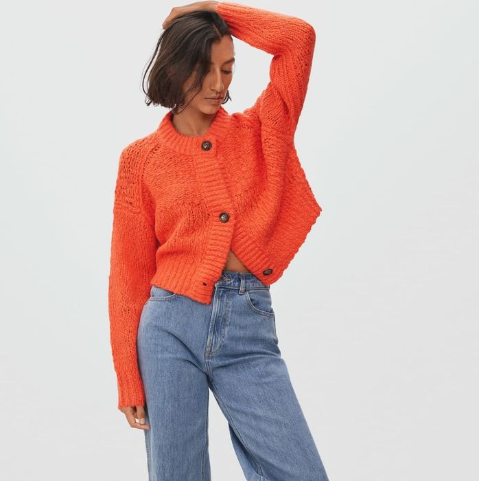 A model sporting the bright orange sweater with bold, chunky buttons