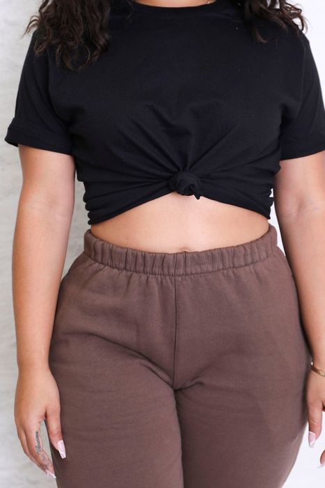 A close-up shot of a model wearing a black knotted crop tee paired with brown sweatpants